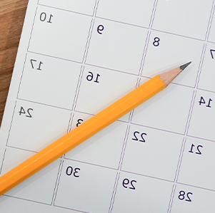 Paper calendar with pencil laid across it on a desk